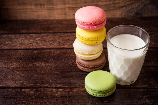 Macarons coloridos e vidro de leite no fundo de madeira escura — Fotografia de Stock