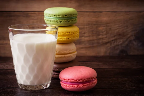 Macarons coloridos e vidro de leite no fundo de madeira escura — Fotografia de Stock