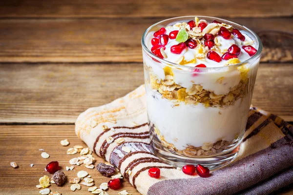 Gezond ontbijt met yoghurt, muesli en granaatappel zaden in glas op houten achtergrond — Stockfoto
