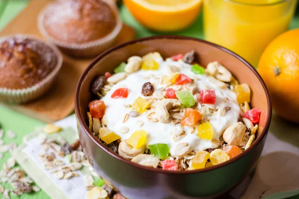 Здоровый завтрак с йогуртом, мюсли и засахаренными фруктами в керамической миске на зеленом деревянном фоне — стоковое фото