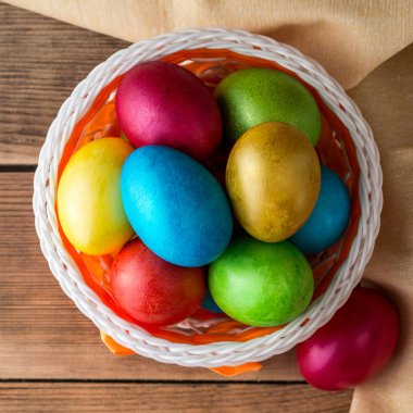 Rustik ahşap masa üzerinde sepetteki renkli boyalı Paskalya yumurtaları.