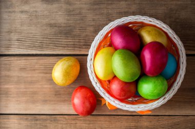 Rustik ahşap masa üzerinde sepetteki renkli boyalı Paskalya yumurtaları.