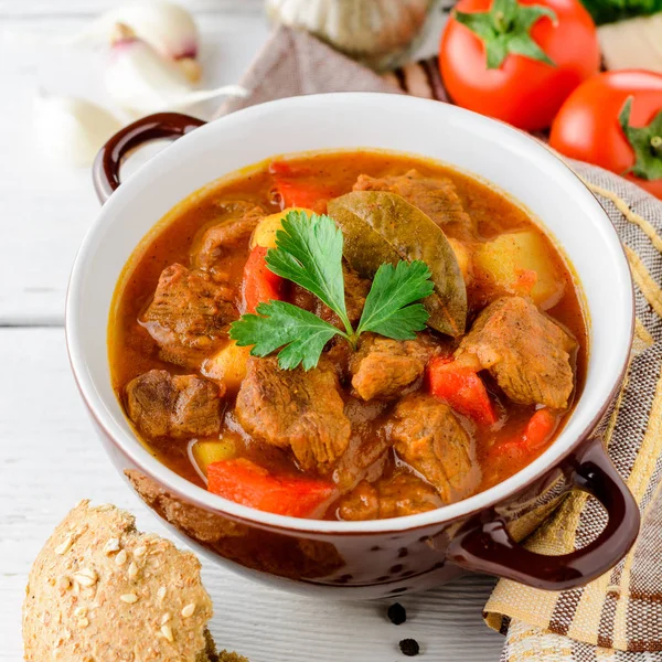 Gulasch in Keramikschale auf weißem Holzgrund. traditionelle ungarische Suppe. — Stockfoto