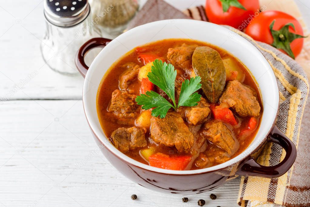 Goulash in ceramic bowl on white wooden background. Traditional hungarian soup.