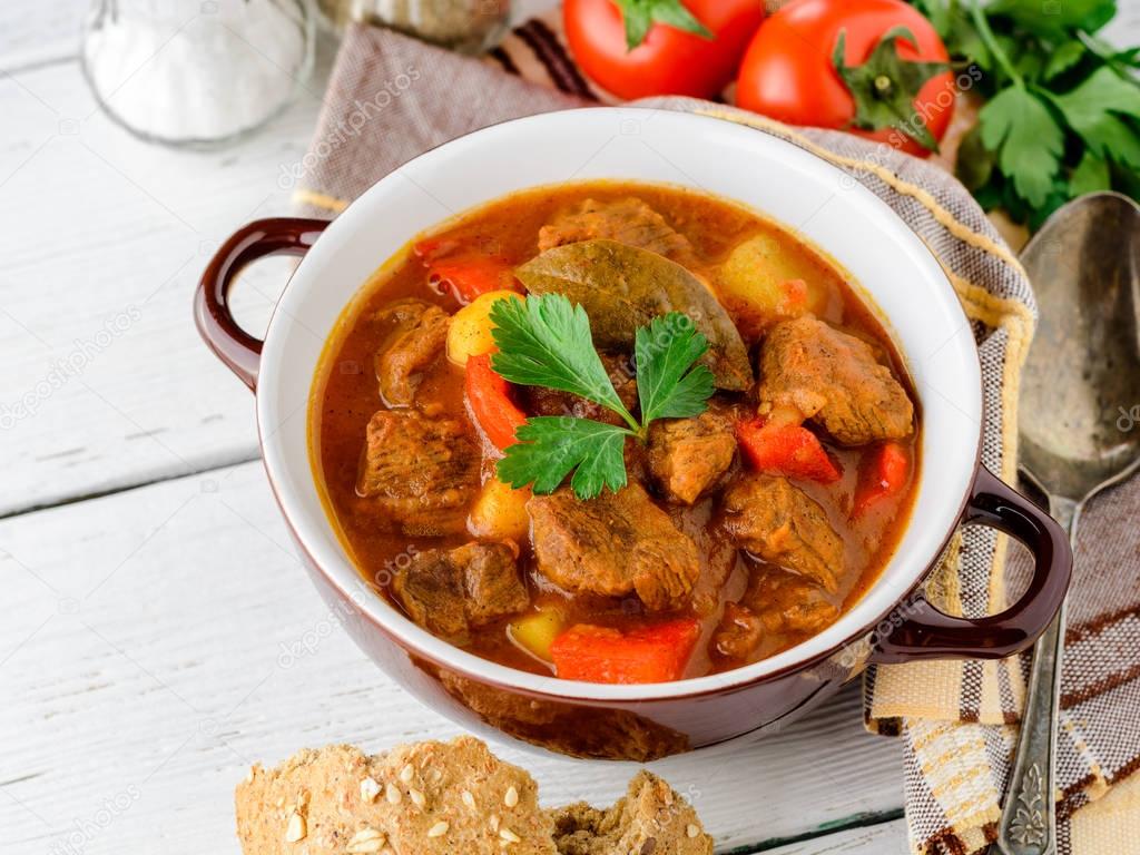 Goulash in ceramic bowl on white wooden background. Traditional hungarian soup.