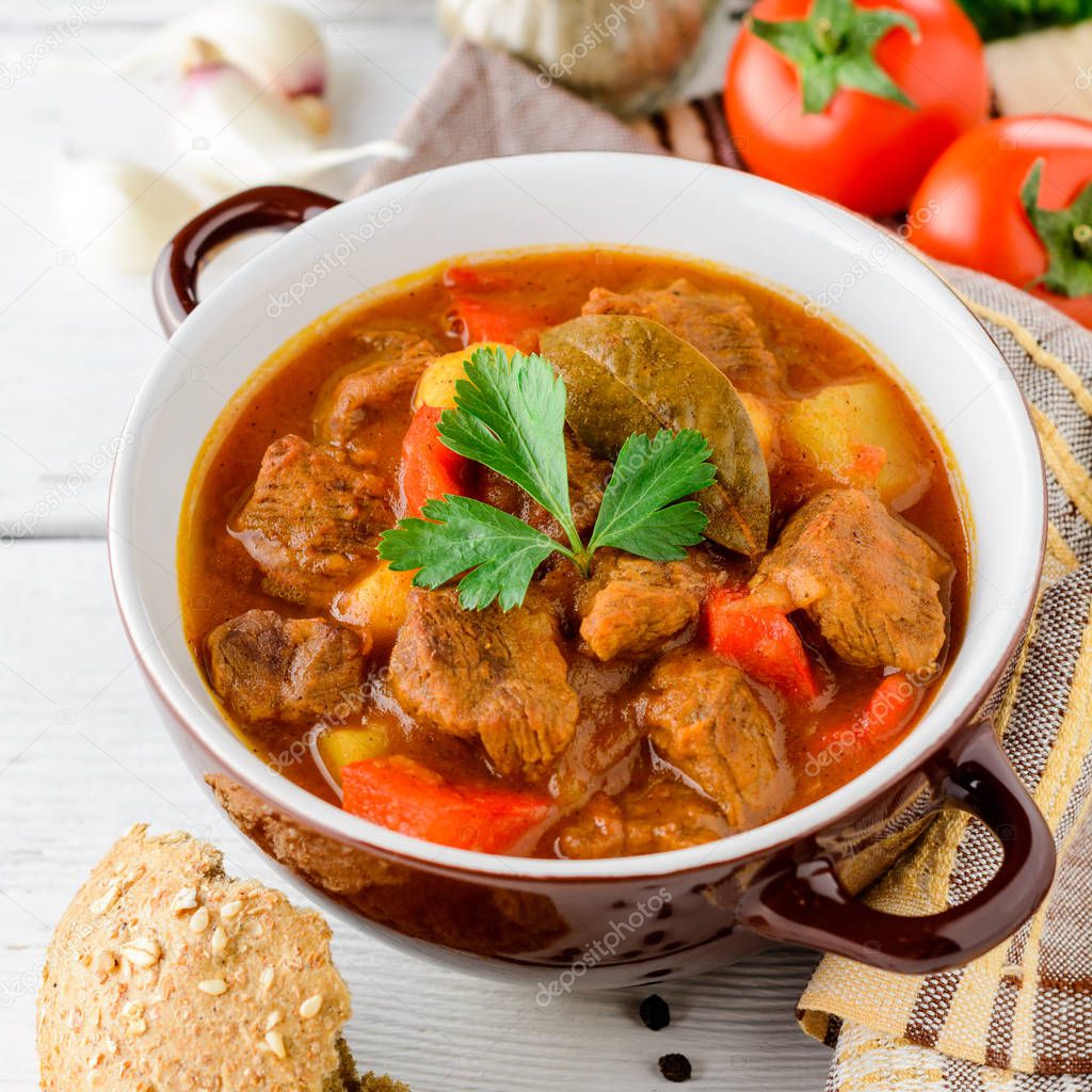 Goulash in ceramic bowl on white wooden background. Traditional hungarian soup.