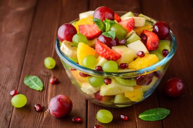 Ahşap arka plan üzerinde cam kapta sağlıklı taze meyve salatası.