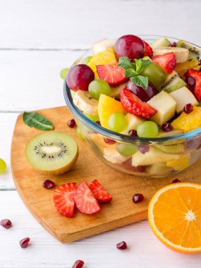 Beyaz ahşap zemin üzerinde cam kapta sağlıklı taze meyve salatası.