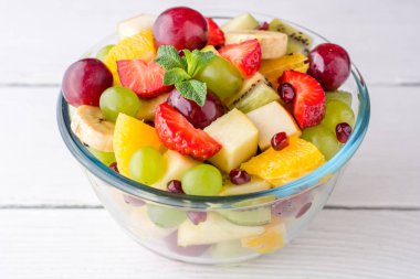 Beyaz ahşap zemin üzerinde cam kapta sağlıklı taze meyve salatası.