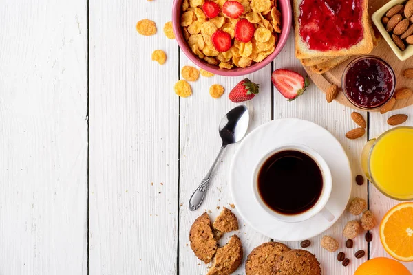 Mesa de pequeno-almoço com ingredientes saudáveis saborosos. Café, torrada, geléia, flocos de milho, biscoitos, amêndoas, suco de laranja e frutas em fundo de madeira branca . — Fotografia de Stock
