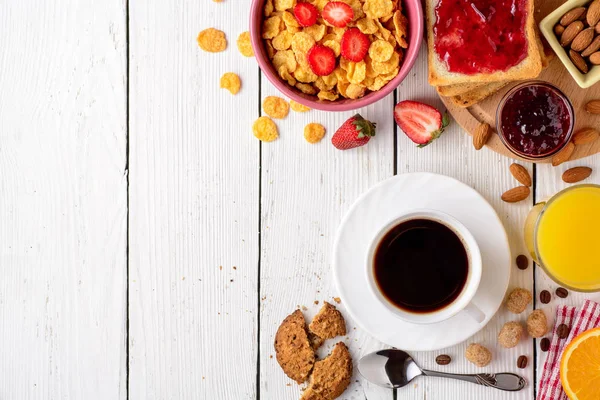 Mesa de pequeno-almoço com ingredientes saudáveis saborosos. Café, torrada, geléia, flocos de milho, biscoitos, amêndoas, suco de laranja e frutas em fundo de madeira branca . — Fotografia de Stock