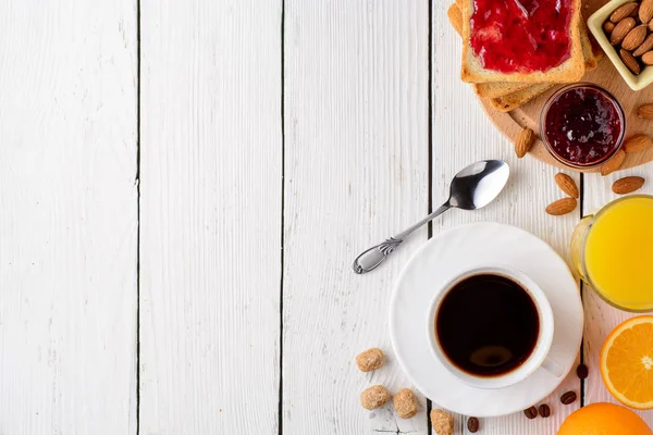 Mesa de pequeno-almoço com ingredientes saudáveis saborosos. Café, torrada, geléia, amêndoas, suco de laranja e frutas sobre fundo branco de madeira . — Fotografia de Stock