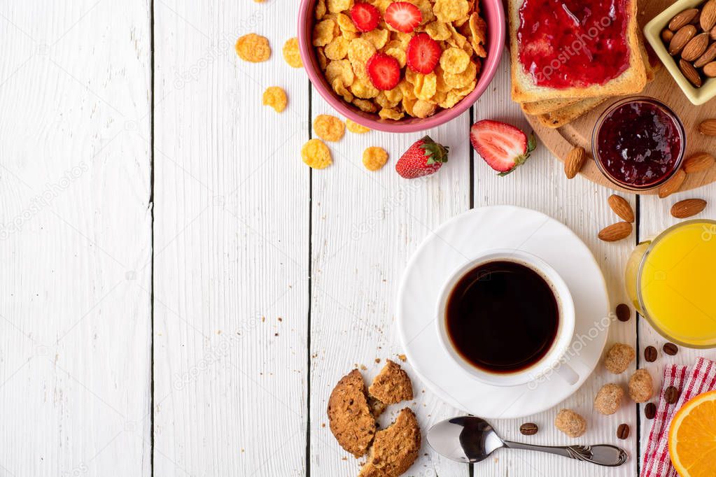 Breakfast table with healthy tasty ingredients. Coffee, toast, jam, corn flakes, cookies, almonds, orange juice and fruit on white wooden background.