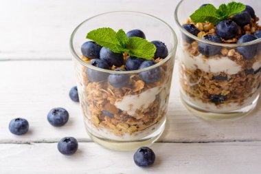 Granola cam Beyaz ahşap masa üzerinde bir yaban mersini ve yoğurt ile.