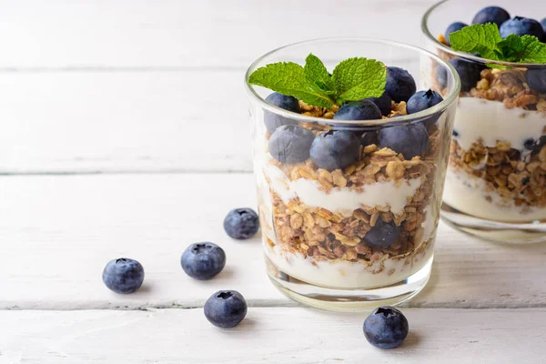 Muesli met yoghurt en bosbessen in glas op witte houten tafel. — Stockfoto