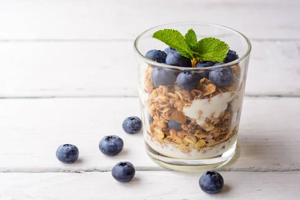 Muesli met yoghurt en bosbessen in glas op witte houten tafel. — Stockfoto