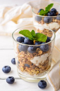 Granola cam Beyaz ahşap masa üzerinde bir yaban mersini ve yoğurt ile.