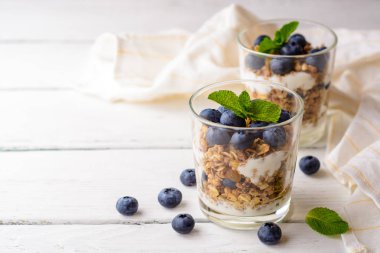 Granola cam Beyaz ahşap masa üzerinde bir yaban mersini ve yoğurt ile.