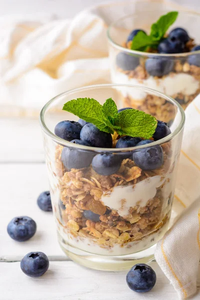 Muesli met yoghurt en bosbessen in glas op witte houten tafel. — Stockfoto