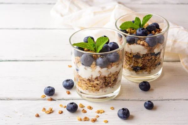 Muesli met yoghurt en bosbessen in glas op witte houten tafel. — Stockfoto