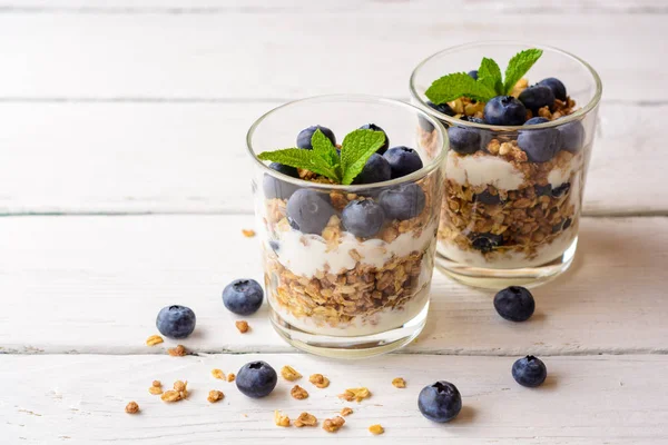 Muesli met yoghurt en bosbessen in glas op witte houten tafel. — Stockfoto