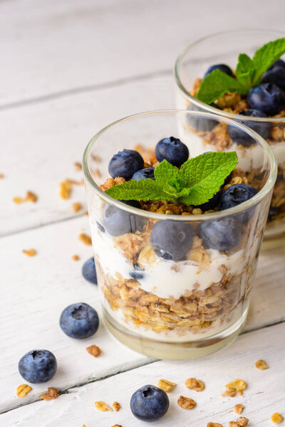 Granola with yogurt and blueberries in glass on white wooden table.