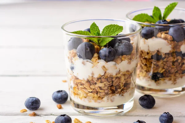 Muesli met yoghurt en bosbessen in glas op witte houten tafel. — Stockfoto