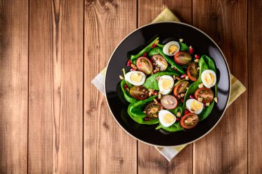 Ispanak, cherry domates, bıldırcın yumurtası, nar taneleri ve ceviz ahşap masa üzerinde siyah plaka ile taze sebze salatası.