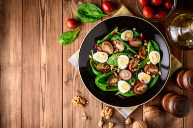 Ispanak, cherry domates, bıldırcın yumurtası, nar taneleri ve ceviz ahşap masa üzerinde siyah plaka ile taze sebze salatası.