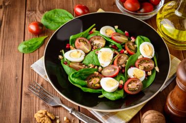 Ispanak, cherry domates, bıldırcın yumurtası, nar taneleri ve ceviz ahşap masa üzerinde siyah plaka ile taze sebze salatası.