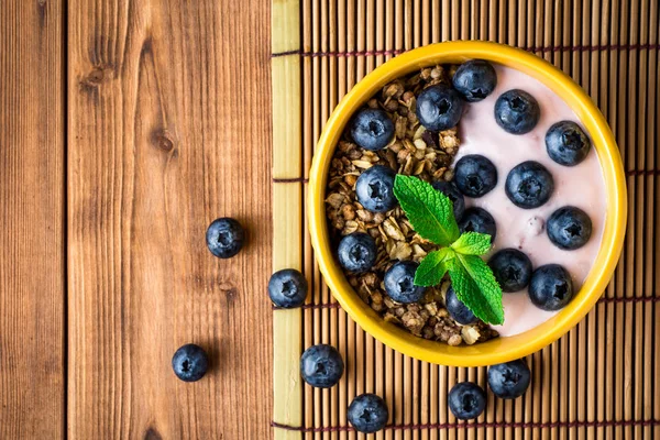 Muesli met bosbessen en yoghurt in de gele kom op houten tafel. — Stockfoto