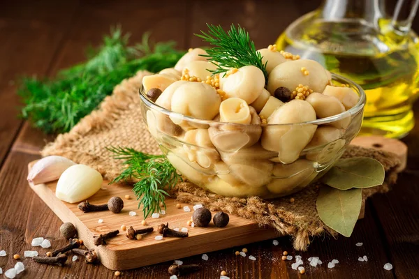 Pickled mushrooms in glass bowl with spices and dill on wooden table. — Stock Photo, Image