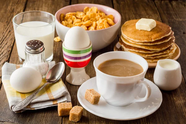 Mesa de café da manhã com café, ovos cozidos, panquecas, flocos de milho e leite . — Fotografia de Stock
