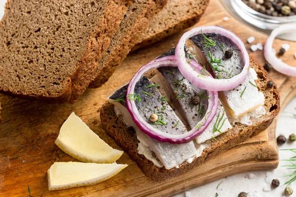 Sandwich met gezouten haring, boter en rode ui op oude rustieke snijplank. — Stockfoto