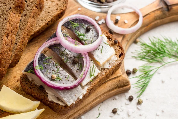 Sandwich met gezouten haring, boter en rode ui op oude rustieke snijplank. — Stockfoto