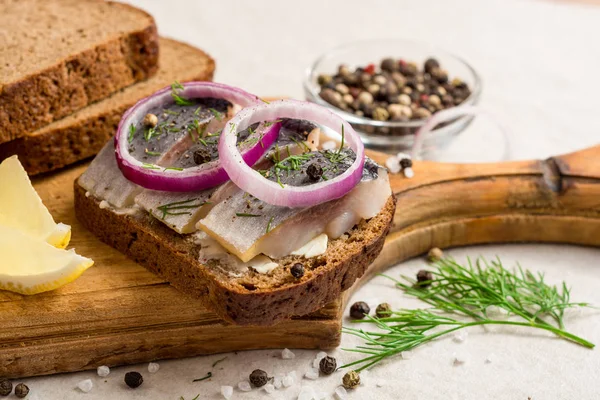 Sandwich met gezouten haring, boter en rode ui op oude rustieke snijplank. — Stockfoto