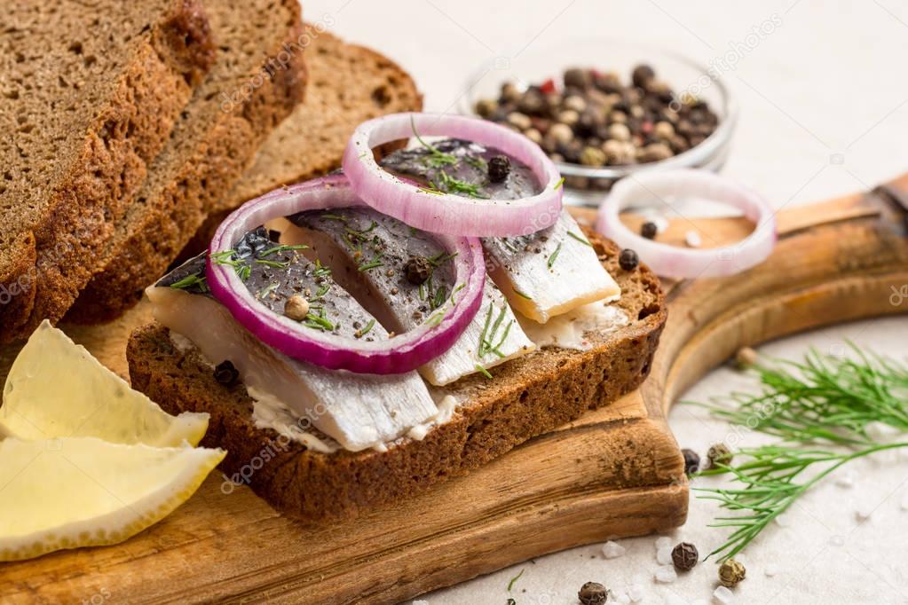 Sandwich with salted herring, butter and red onion on old rustic cutting board.