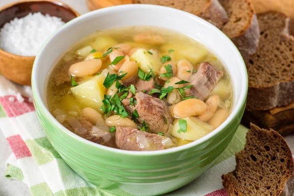 Beef soup with potatoes, beans and leeks in ceramic bowl on stone background. — Stock Photo, Image