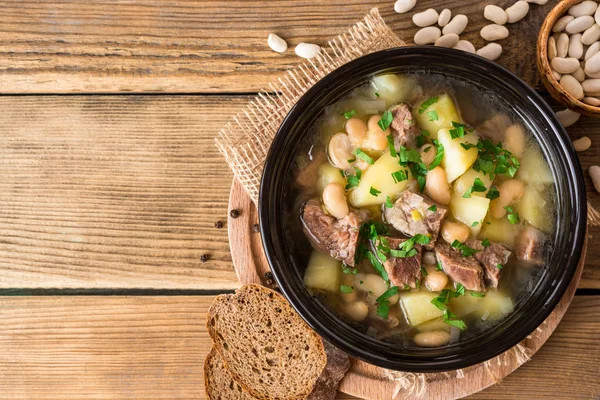 Говяжий суп с картошкой, бобами и луком-порей в керамической миске на каменном фоне . — стоковое фото
