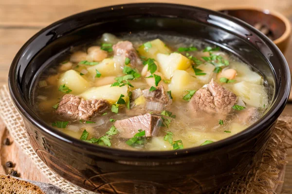 Яловичий суп з картоплею, квасолею і цибулею в керамічній мисці на кам'яному фоні . — стокове фото