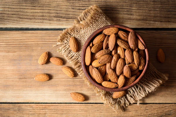 Almonds in ceramic bowl on wooden background — Stock Photo, Image