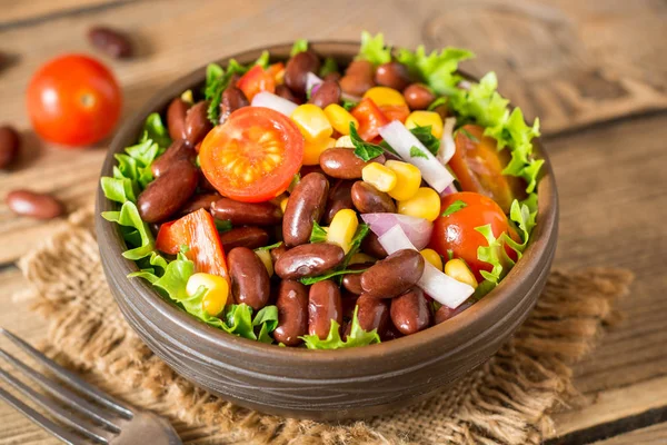 Fasulye ahşap masa üzerinde seramik kase taze sebze salatası.