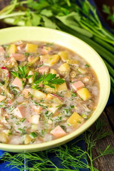 Okroshka. Tradiční ruské letní studená polévka s klobásou, zeleninou a kvas v misce na dřevěné pozadí. — Stock fotografie