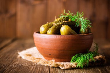 Karanlık rustik ahşap masa üzerinde seramik kase dereotu salatalık turşusu.