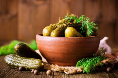 Karanlık rustik ahşap masa üzerinde seramik kase dereotu salatalık turşusu.