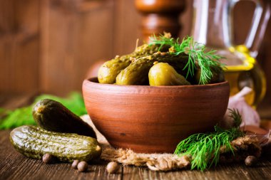 Karanlık rustik ahşap masa üzerinde seramik kase dereotu salatalık turşusu.