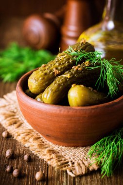 Karanlık rustik ahşap masa üzerinde seramik kase dereotu salatalık turşusu.