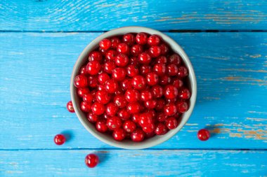 Mavi ahşap zemin üzerine kase taze kırmızı kuş üzümü.