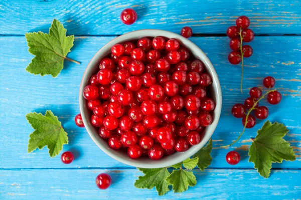 Mavi ahşap zemin üzerine kase taze kırmızı kuş üzümü.