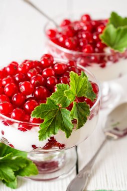 Yoğurt tatlı kırmızı kuş üzümü ile ve Beyaz ahşap zemin üzerinde yapraklarla süslenmiş